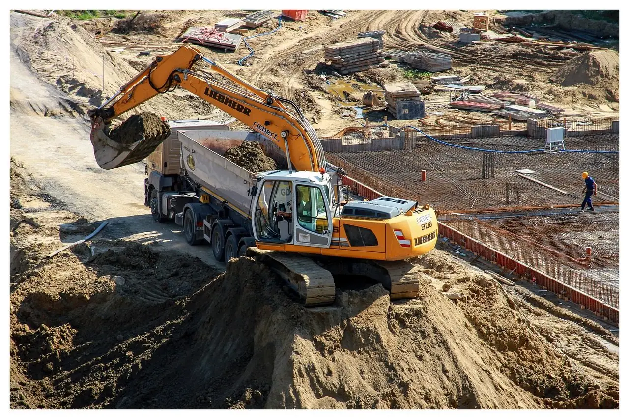 Yellow excavator loading sand into a dump truck on a construction site