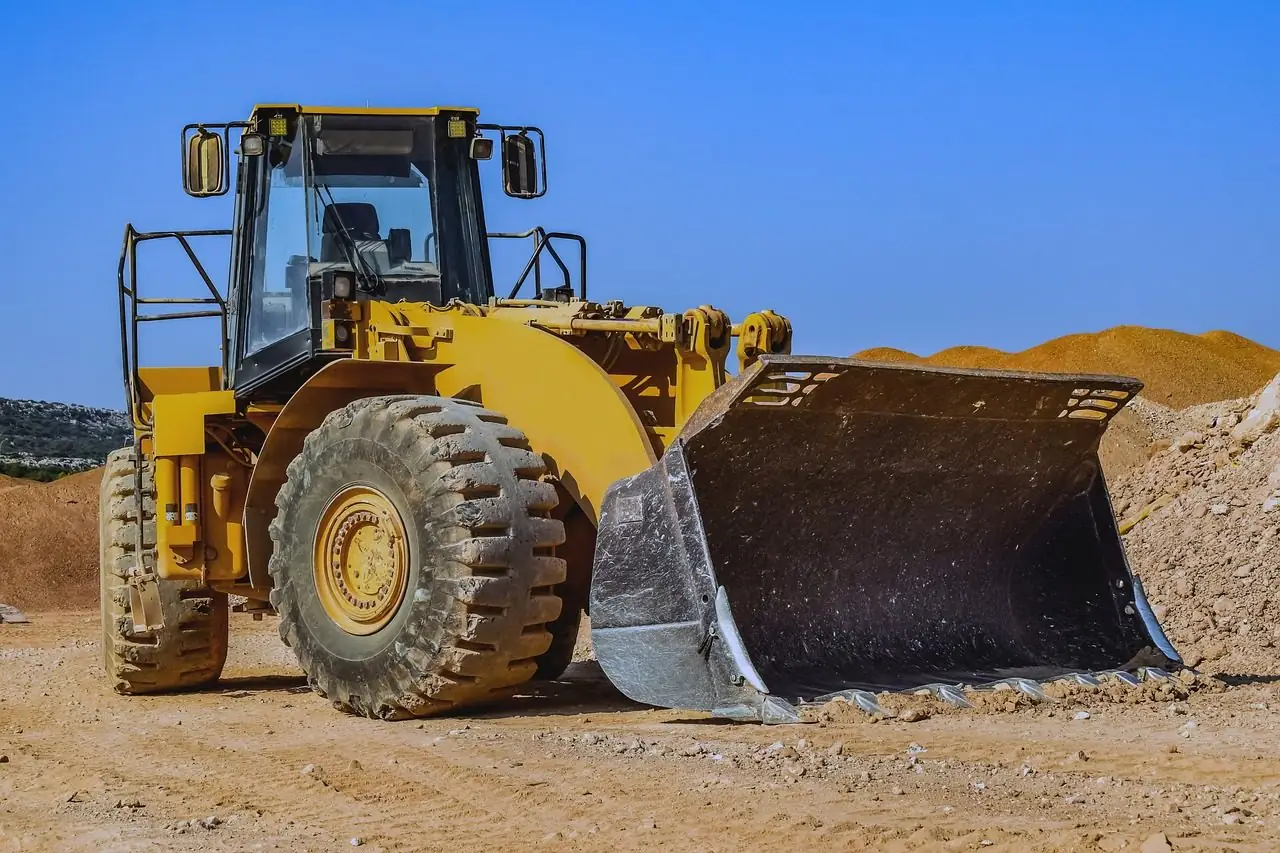 Yellow wheel loader with a raised bucket in front of a sand pile